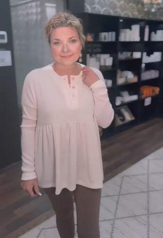 Soft beige babydoll top with long sleeves and button placket, perfect for effortless style and comfort in everyday outfits.