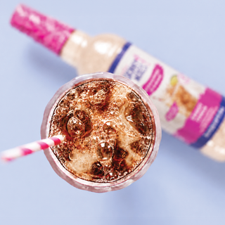 Jordan's Skinny Mixes sweet cream syrup pouring from bottle spout into a small glass with bubbles