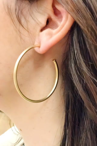 Matte gold hoop earrings on a model's ear, smooth round hoop