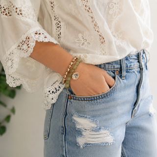 Tan marbled bead stretch bracelet with gold coin crystal charm on arm near denim jeans