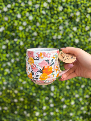Floral ceramic mug with pink handle and “You are loved” charm tag, held up for view