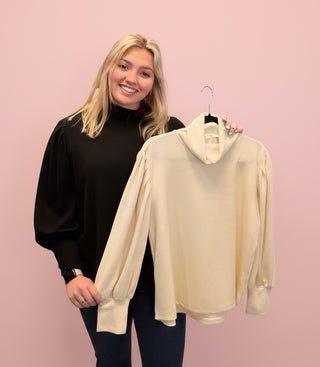 Woman wearing a beige sweater in front of a pink background and a black sweater 