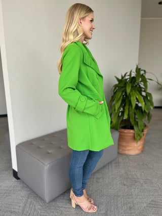 Green long-sleeve coat with button front and flap pockets, side view.