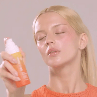 Dr. C. Tuna Glow Face Mist orange bottle with spray nozzle, held in hand