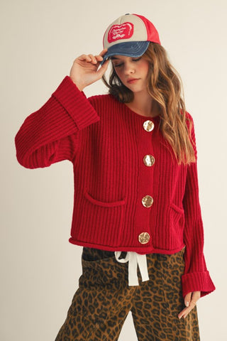 LovLov red ribbed knit cardigan with oversized gold buttons and patch pockets, worn buttoned with a trucker cap and leopard pants – three-quarter front view