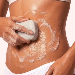 White speckled massage soap held in hands with foamy lather on skin
