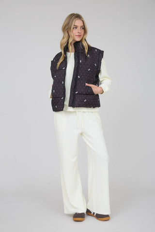 Sleeveless dark puffer vest with high neck and front zipper, small light print pattern