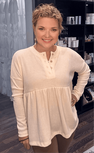 Comfortable babydoll top in soft beige fabric with button neckline, styled for casual wear in a beauty boutique setting.