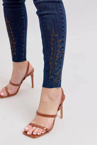 Close-up of ankle embroidery on Judy Blue Plus Size High Rise Skinny Jeans, featuring brown stitching on dark denim for a chic finish.
