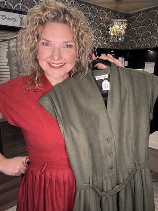 Close-up of the Olive pinwale corduroy dress with button front and tie belt, held by a model in Wine
