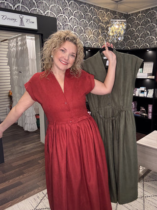 Wine pinwale corduroy belted midi dress on a model, with the Olive color on a hanger beside her