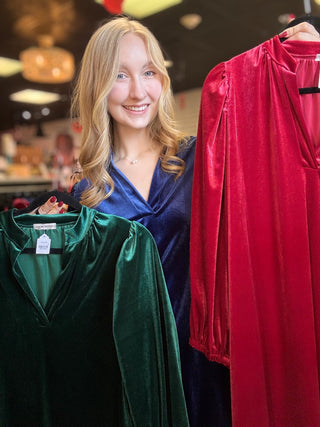 Carole Christian velvet balloon sleeve V-neck dresses in Green and True Red on hangers, held by a model wearing Navy